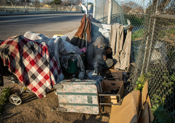 a person experiencing homelessness makes a fire next to their makeshift tent