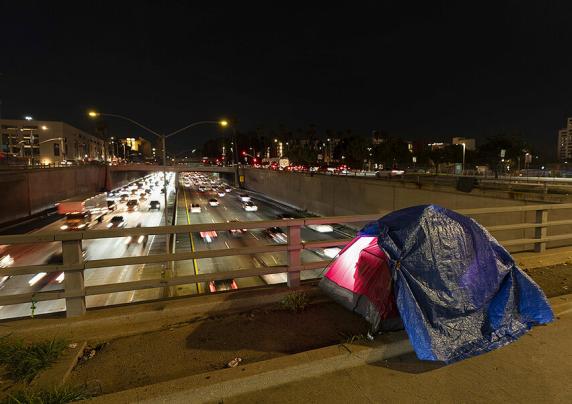A tarp covers a portion of a person experiencing homelessness's tent on a bridge overlooking a freeway