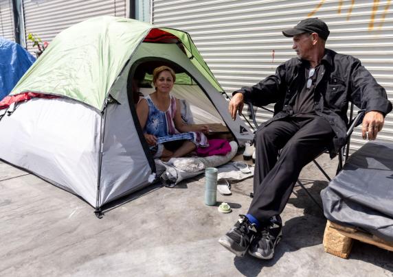 two people next to a garage. one person is in a tent, the other is sitting in a chair