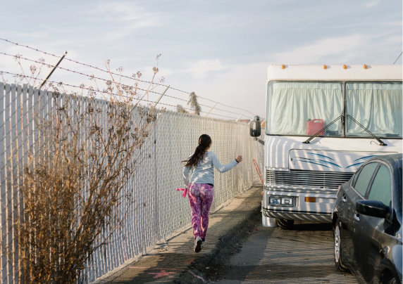 Photo of a girl running next to a fence and a mobile home