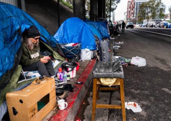 a person experiencing homelessness sitting near a makeshift tent on the sidewalk