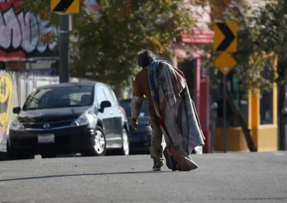 A man walks down the street carrying a blanket