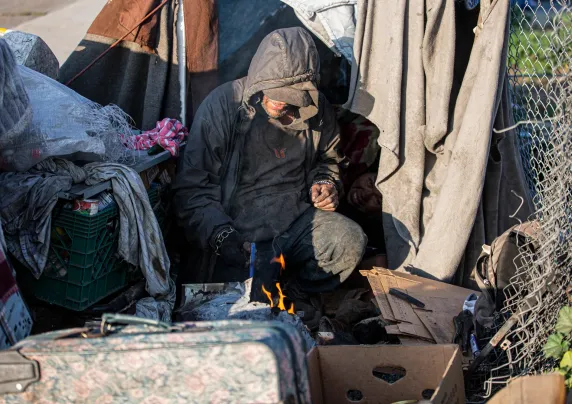 an individual experiencing homelessness is resting near tents.