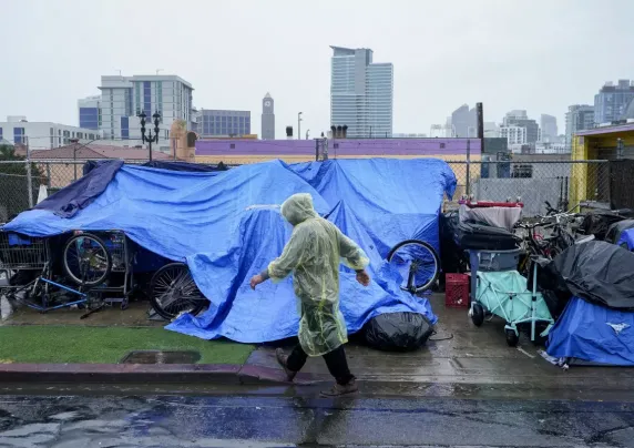 Large tarps cover belongings in the rain on a city sidewalk