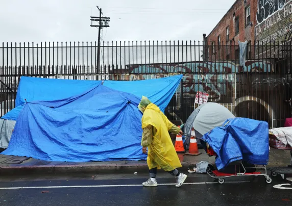 Person pulls a shopping cart past tents on a sidewalk