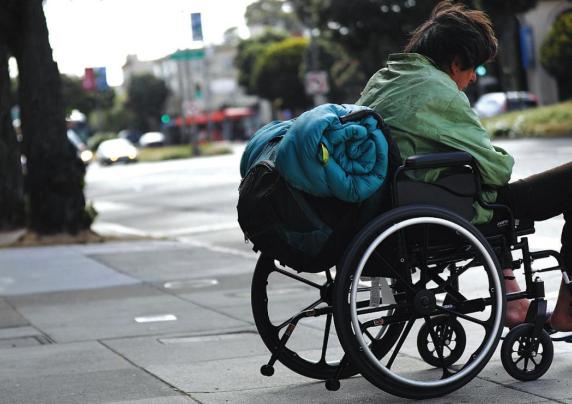 A homeless man in a wheelchair on a city sidewalk