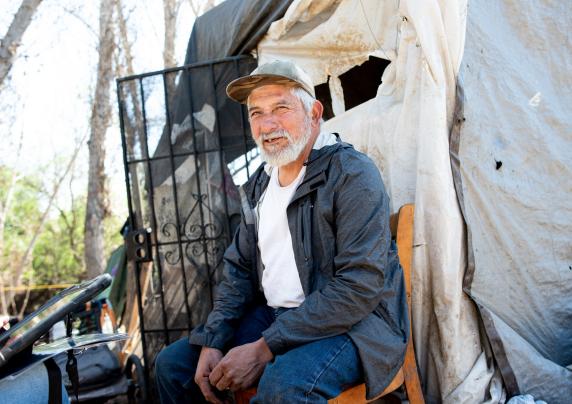 Elderly gentlemen sitting on a chair in front of his encampment