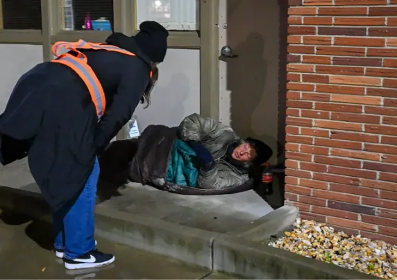An outreach worker speaks with a person sleeping on the sidewalk