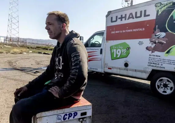 A man sits outside on a box near a moving truck