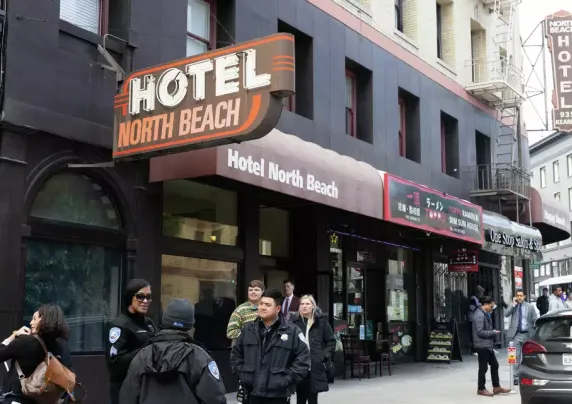 People and police officers stand on the sidewalk outside a hotel