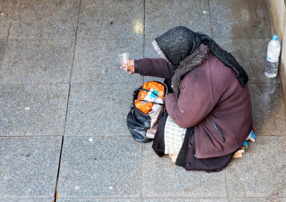 photo of older woman bundled up sitting on a sidewalk