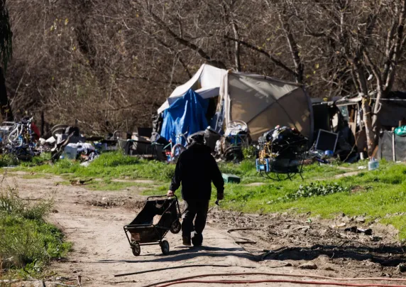 Photo of man pulling a wagon at a homeless encampment