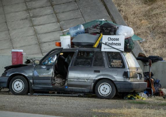 A man lounging in a chair next to his car, piled high with his belongings