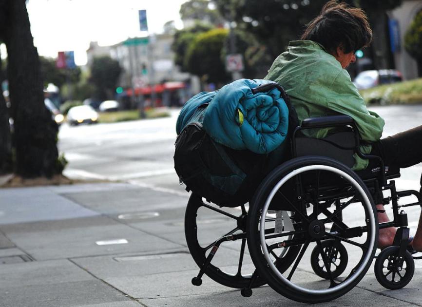A homeless man in a wheelchair on a city sidewalk