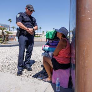  Photo of police officer speaking with homeless woman sitting in the shade of a bus stop